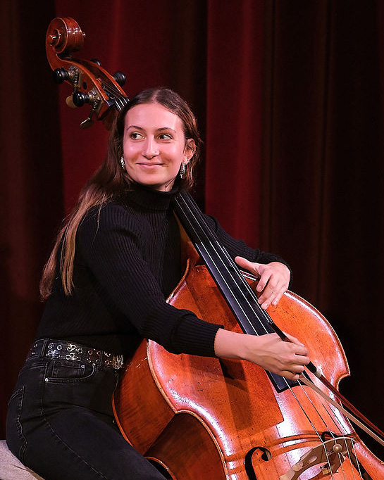 A female cellist, wearing a black top and black trousers, looking beyond the sta